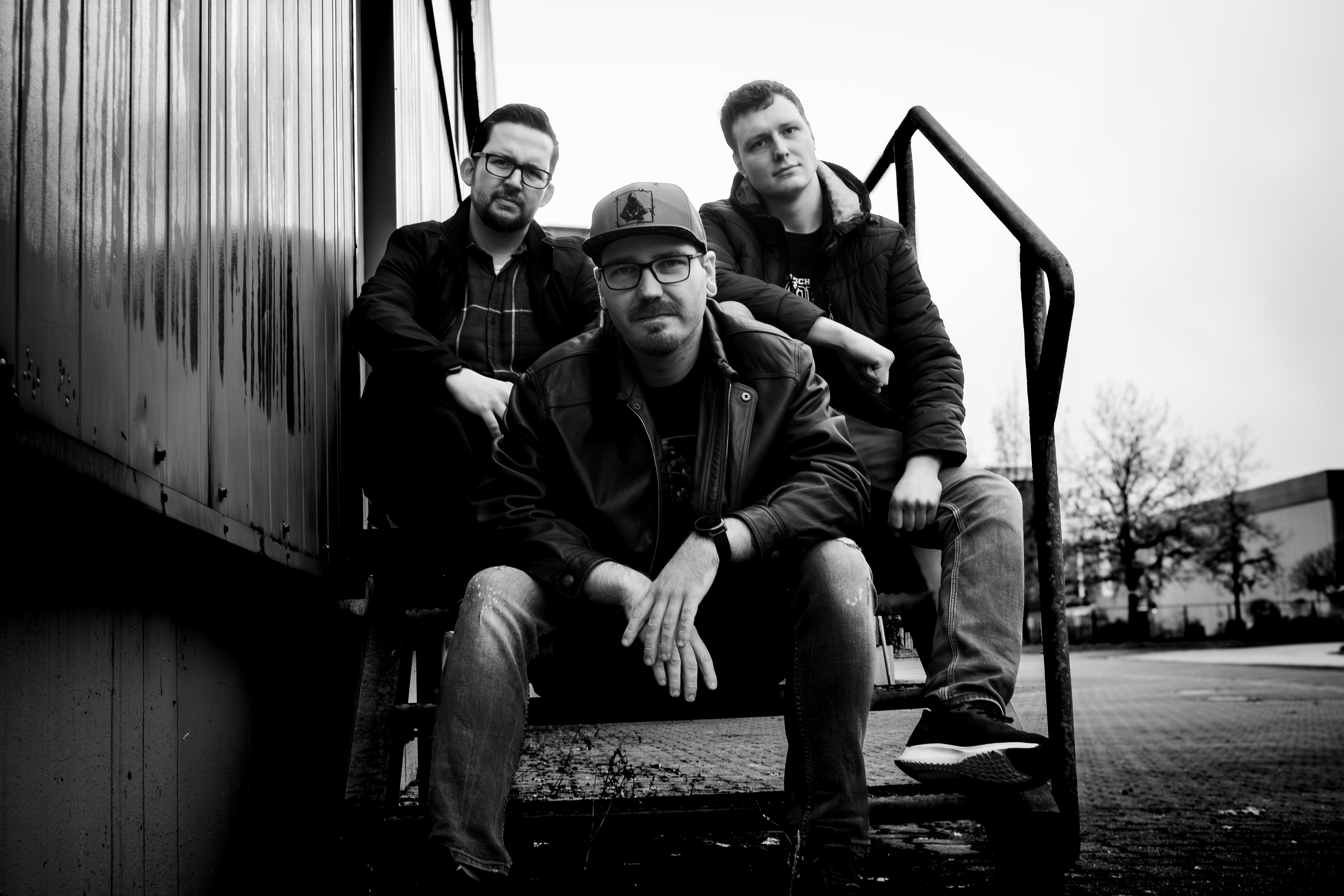 Kein Garten Verein: Marv, Chrischi und Adrian stehen auf einem Geländer vor einer grünen Wellblechfassade und blicken selbstbewusst zur Seite.